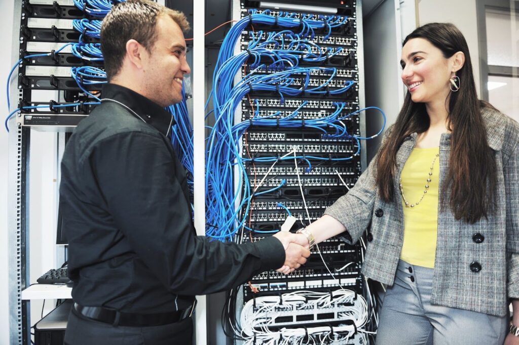 Two professionals shake hands in front of organized server rack.