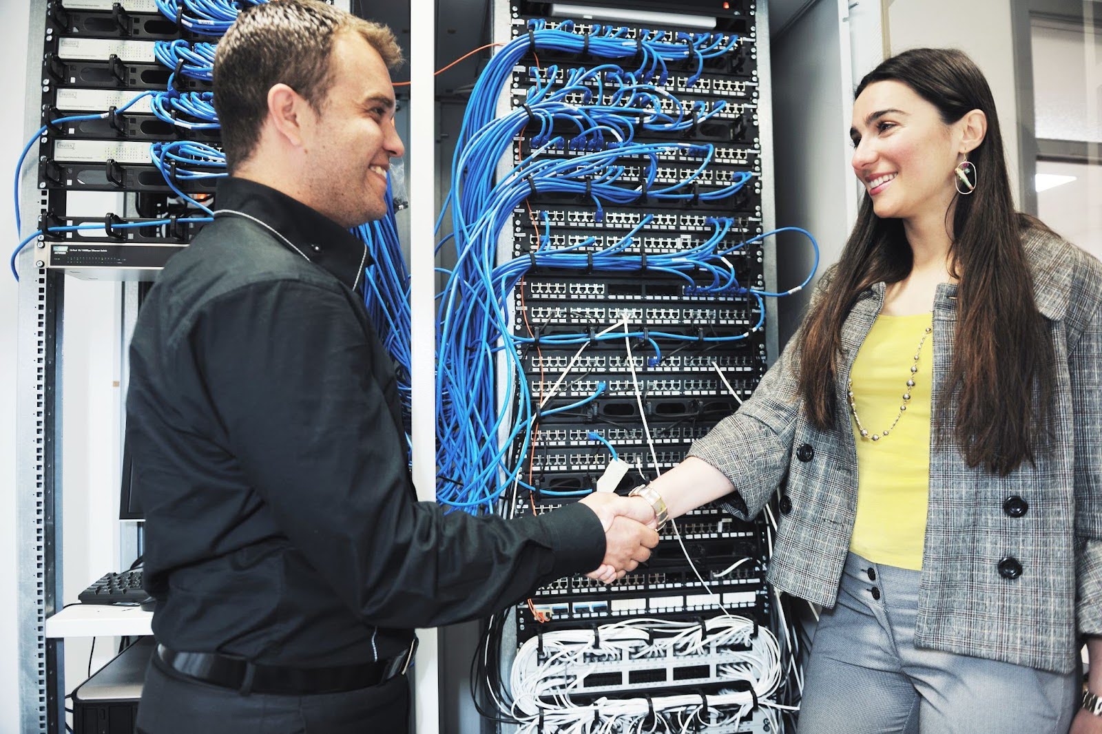 Two professionals shake hands in front of organized server rack.