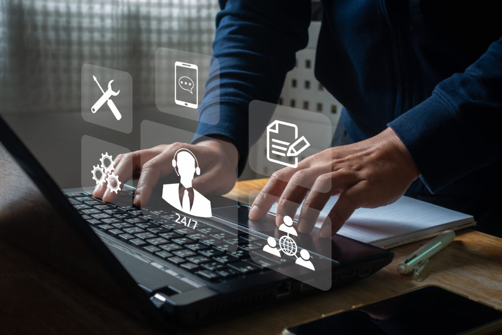 Person typing on a laptop at a desk with digital icons representing tech support and communication tools.